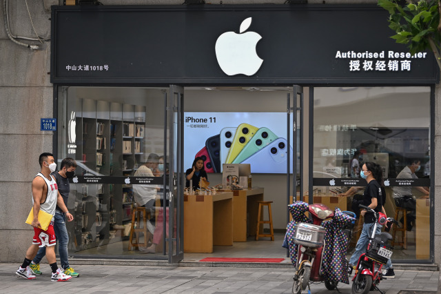 People wearing face masks walk past an Apple store in Wuhan, in Chinas central Hubei province on May 26, 2020. (Photo by Hector RETAMAL / AFP) (Photo by HECTOR RETAMAL/AFP via Getty Images)