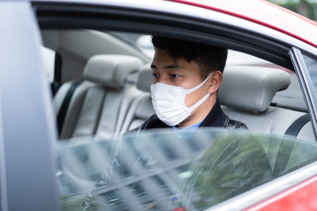 شاب آسيوي يرتدي قناع الوجه للحماية والوقاية من انتشار الفيروسات في السيارة