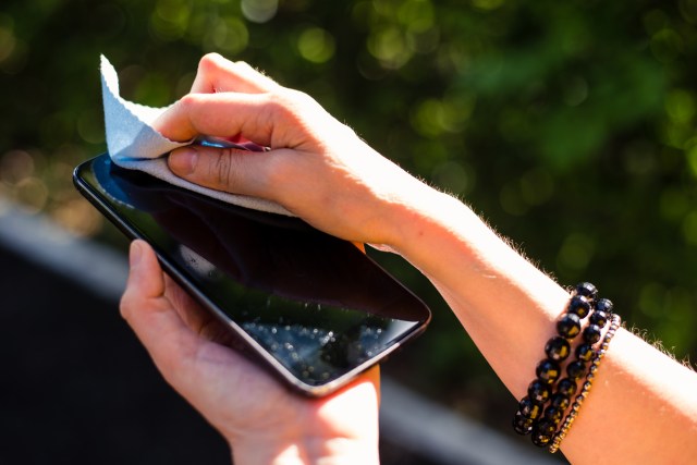 Young person’s hands holding black smartphone while cleaning it with blue cloth – Young female washing mobile phone screen with soft fabric from dust