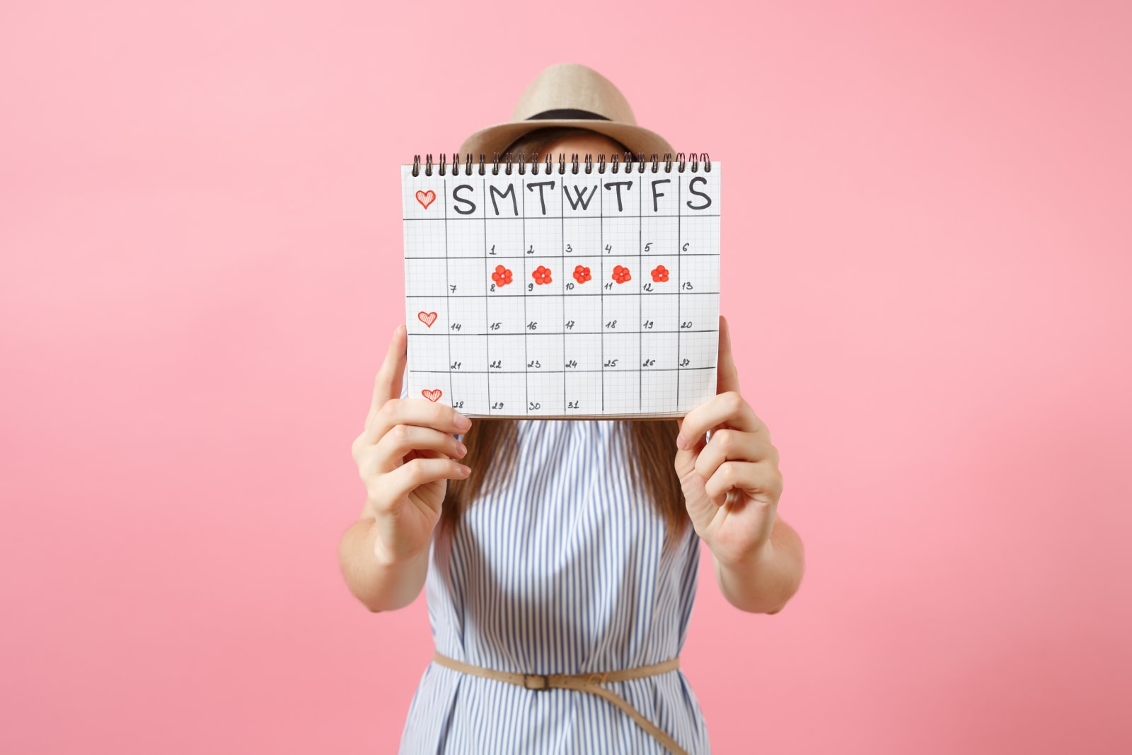 Portrait of woman in blue dress cover face, hiding behind periods calendar for checking menstruation days isolated on trending pink background. Medical, healthcare, gynecological concept. Copy space.